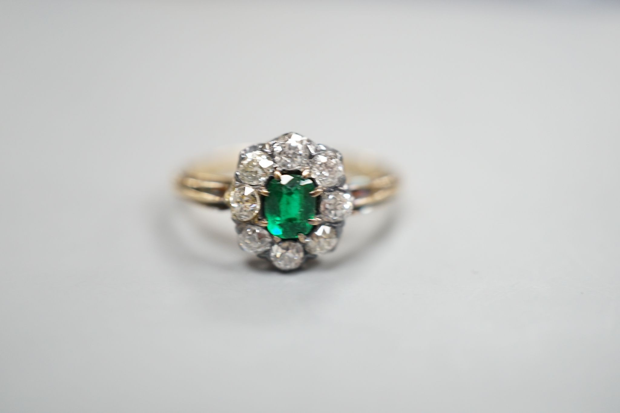 A yellow metal, emerald and diamond set oval cluster ring, size M/N, gross weight 3.1 grams.